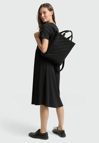 Schwarze, gesteppte Tragetasche mit doppelt getragenen Schulterriemen, die ein geometrisches Muster zeigt. Trägt man über einem schwarzen Kleid, das ein minimalistisches Design zur Schau stellt.
