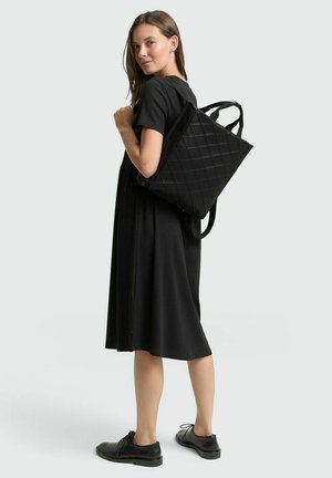 Zwarte gewatteerde tote bag met dubbele schouderbanden, met een geometrisch patroon. Draagt over een zwarte jurk, wat een minimalistisch ontwerp benadrukt.