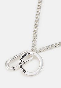 Colar de corrente de metal prateado com um pendente redondo e um mosquetão com fecho, gravado com coordenadas e a palavra "ICON".