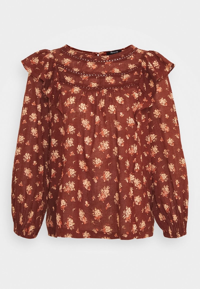 Blouse florale marron avec des épaules à volants, des manches longues et un tissu texturé. Présente de petits motifs de fleurs crème et rose sur un fond sombre.