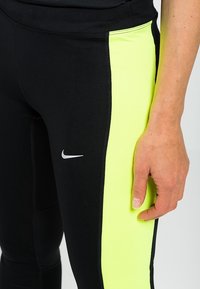 Leggings neri con un pannello laterale di un vivace verde lime e il logo Nike in argento. Presentano una vestibilità aderente e un tessuto elasticizzato per il movimento.