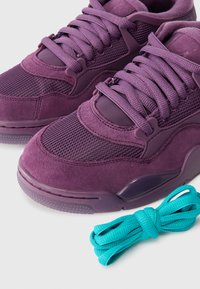 Μωβ σουέτ και δίχτυνα αθλητικά παπούτσια με τονισμένη ελαστική σόλα. Περιλαμβάνουν τιρκουάζ κορδόνια. Διαθέτουν επίπεδα κορδόνια και υφές.