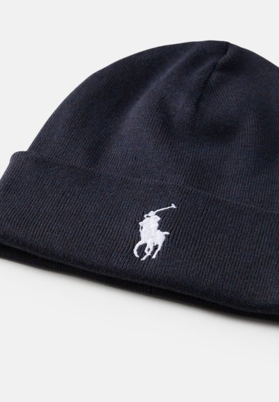 Gorro de malha azul-marinho escuro com textura canelada, apresentando um logotipo de polo bordado em branco na parte frontal e um design de aba dobrada.