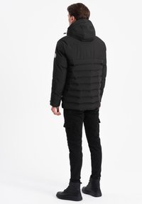 Svart puffjacka med en åtsittande design, ribbad textur och huva. Tillsammans med svarta cargo-byxor och snörade kängor.