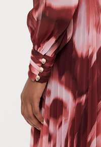 Langärmliges Kleid in Farbverläufen von Burgunderrot und Pink. Mit plissiertem Textur und einem Bund mit drei goldfarbenen Knöpfen.
