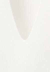 Gros plan sur un tissu blanc côtelé avec un décolleté en V profond, montrant la texture et le motif tricoté.
