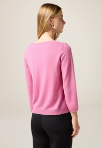 Suéter rosa ligero de punto suave, con cuello redondo y mangas de tres cuartos, combinado con pantalones negros para un contraste.