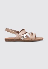 Sandalias de tiras hechas de cuero beige con acentos plateados, que cuentan con una suela plana y una correa trasera con hebilla. Las tiras cruzadas añaden textura.