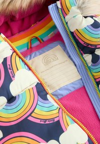 Abrigo acolchado con patrones de arcoíris multicolor y nubes. Presenta un forro de forro polar rosa y una etiqueta para detalles personales. Cierre con cremallera.
