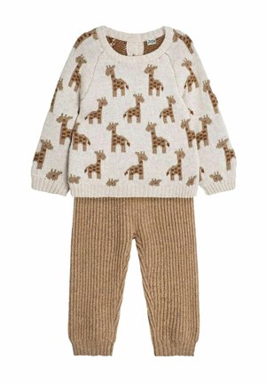 Pull en tricot avec une base crème et un motif de girafe marron, associé à un pantalon beige texturé et côtelé. Tissu léger, ensemble décontracté.