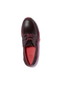 Chaussure en cuir marron foncé avec des accents rouges, bout rond et design à lacets. Présente une couture contrastante et une semelle intérieure texturée.