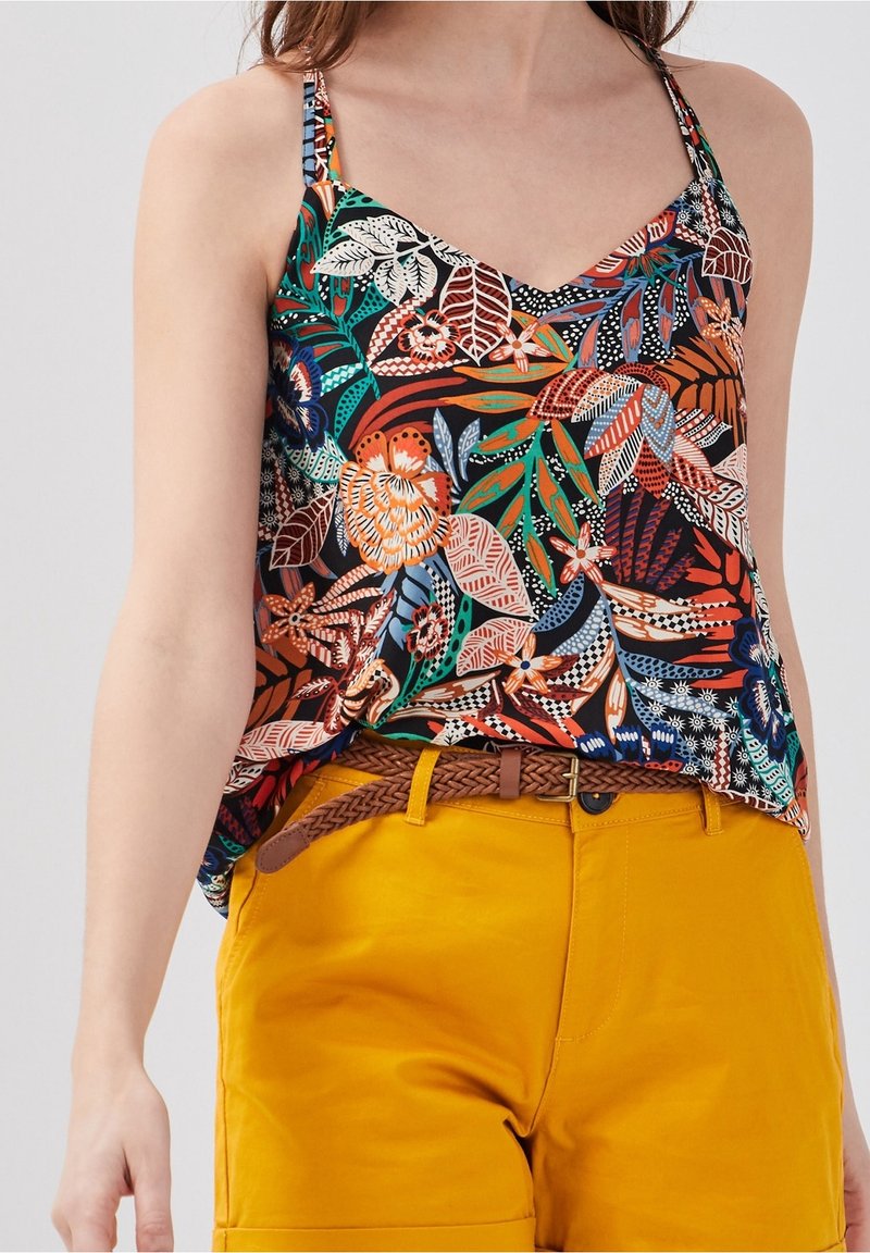 Femme portant un haut sans manches à motif floral avec de fines bretelles, associé à un short jaune moutarde et une ceinture tressée marron.