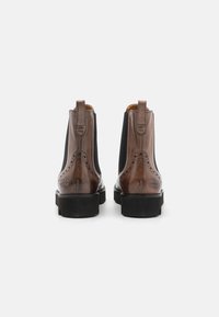 Brune skinn Chelsea-støvler med sorte elastiske sider, broguedetaljer, drahanker og gummisåle, vist fra bakvinkel.