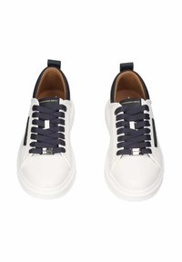 Zapatillas blancas con cordones azul marino, de material de cuero, punta redondeada y etiqueta en el lateral. Presentan un diseño de perfil bajo y acentos en contraste.