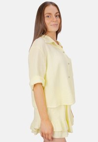 Chemise jaune, texturée, à manches courtes et à boutons sur le devant avec une coupe loose, assortie d'une jupe à volants qui lui correspond.