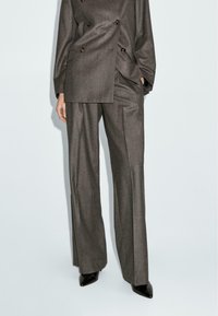 Braun maßgeschneiderter doppelreihiger Blazer mit goldenen Knöpfen, kombiniert mit passenden weiten Hosen. Schwarze spitze Pumps runden den Look ab.