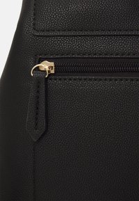 Svart faux läderhandväska med texturerad yta, guldfärgad dragkedja och en ficka med platt flik för enkel öppning.