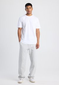 T-shirt blanc à col rond, pantalon de survêtement gris avec taille élastique, et baskets blanches. Design simple, coupe décontractée, en mélange de coton.