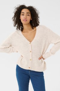 Ljus beige cardigan med djup V-ringning, ribbade nederkanter och tr�äknappar. Mjuk textur, avslappnad passform och långa ärmar, kombinerad med blåjeans.