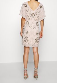 Kort rosa klänning med v-formad rygg, korta flygande ärmar, prydd med intrikata guldpärlor och blommig broderi. Till detta bärs ljusgrå remsandaler.