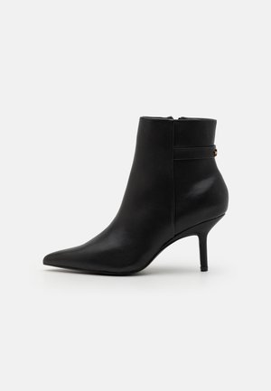 Bottine en cuir noir à bout pointu avec un talon stiletto fin de hauteur moyenne et une fermeture éclair latérale, présentée sur un fond uni.