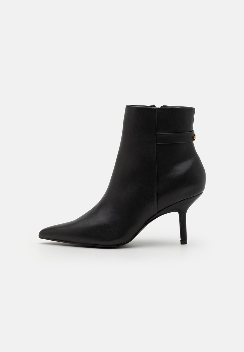 Bottine en cuir noir à bout pointu avec un talon stiletto fin de hauteur moyenne et une fermeture éclair latérale, présentée sur un fond uni.