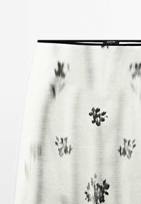 Jupe blanche avec des motifs floraux abstraits noirs et une fine ceinture noire, étiquetée Massimo Dutti.