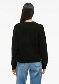 Pull en tricot noir à manches longues, coupe décontractée, et col rond. Associé à un jean en denim bleu clair.