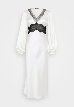 Robe en satin blanc avec manches longues bouffantes et détails en dentelle noire au niveau du décolleté et du buste. Texture lisse, silhouette ajustée.