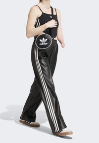 Svarta läderbyxor med vita sidostreck, ihopparade med en svart linne och en rund svart axelväska med Adidas-logotypen.