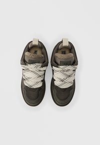 Ζευγάρι από καφέ και μπεζ αθλητικά παπούτσια UGG με χοντρά κορδόνια με σχέδιο και μαλακή επένδυση, σε θέαση από πάνω σε λευκό φόντο.