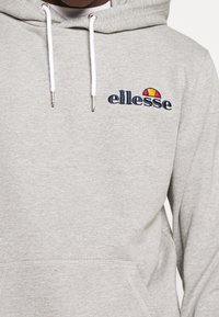 Sweat à capuche gris en tissu doux, doté d'une poche avant, de cordons blancs et d'un logo brodé en bleu marine avec un accent coloré.