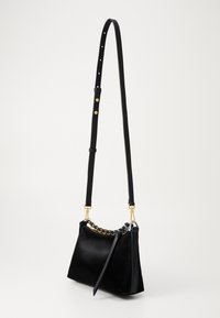 Borsa a tracolla in pelle nera con tracolla regolabile, dettaglio in catena dorata e cursore della cerniera in oro su sfondo bianco.