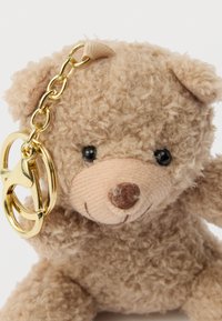 Brown plush teddy bear keychain with a fuzzy texture, black eyes, a stitched nose, and a gold metal chain attached to its head.