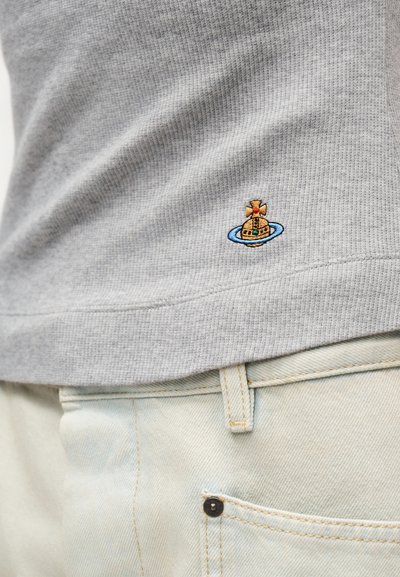 Γκρι πουλόβερ από ύφασμα βάφλ, με μικρό κεντητό χρυσό σφαιρικό και μπλε λογότυπο δακτυλίου, σε συνδυασμό με ανοιχτόχρωμο τζιν παντελόνι.