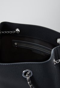 Sac fourre-tout noir texturé avec une anse en chaîne métallique, quincaillerie argentée, et une poche zippée à l'intérieur, avec un doublage lisse et une étiquette de logo.