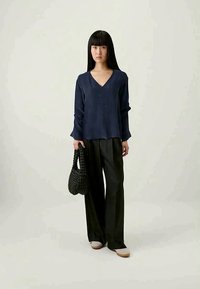 Navy blue V-neck blouse with long sleeves, paired with black wide-leg pants. Holding a textured black handbag, featuring a smooth fabric.