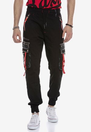 Jogging pants cargo noirs avec plusieurs poches zippées, accents rouges et poignets élastiques. Comprend un panneau noir brillant et une finition texturée.