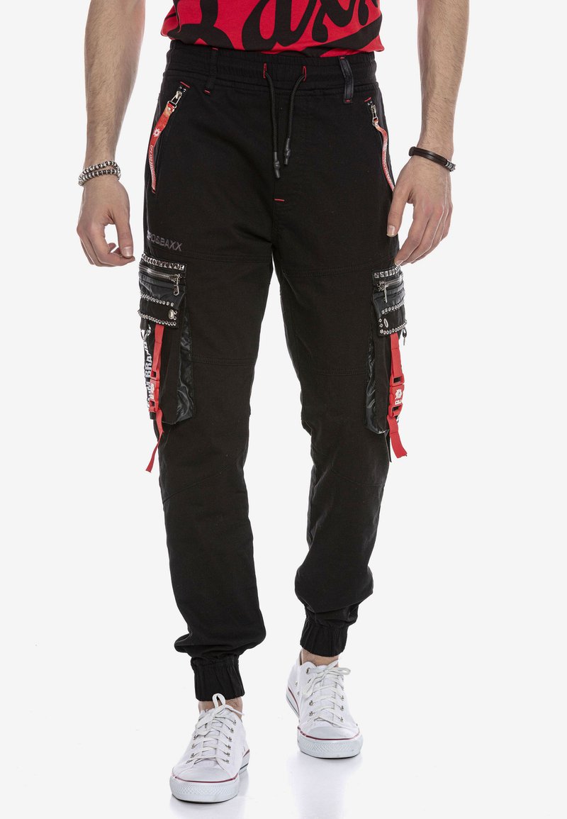 Schwarze Cargo-Jogginghose mit mehreren Reißverschlusstaschen, roten Akzenten und elastischen Bündchen. Verfügt über ein glänzendes schwarzes Panel und eine strukturierte Oberfläche.