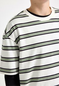 Kortærmet T-shirt i hvid bomuld med sorte og grønne vandrette striber. Har rund halsudskæring og afslappet pasform.