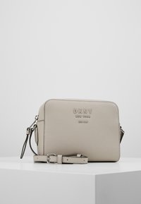 Borsa a tracolla in pelle grigia chiaro con texture e tracolla regolabile. Presenta logo in rilievo, chiusura con zip e forma rettangolare.