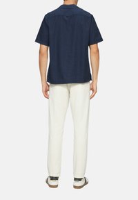 Kurzärmeliges navy-blaues Hemd mit strukturierter Oberfläche, Rückenteil mit Yoke-Detail, kombiniert mit cremefarbenen Hosen und weißen Sneakers mit braunen Sohlen.