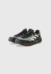 GORE-TEX pohodni čevlji v temno zeleni barvi z odsevnimi belimi črtami, črnimi vezalkami, teksturiranimi podplati in oranžnimi detajli na podplatu.