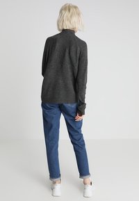 Ciemnoszary, prążkowany sweter z wysokim dekoltem i długimi rękawami, połączony z luźnymi niebieskimi dżinsami i białymi trampkami. Prosty, fakturowany wzór.