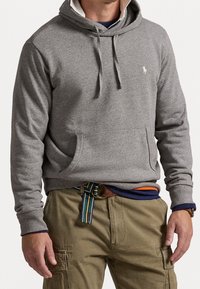 Grå bomullshoodie med dragsko i luvan, framficka och broderad logotyp. Bärs med khakifärgade cargobyxor och ett mångfärgat bälte.