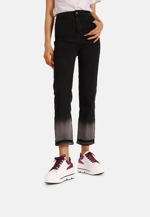 Jeans neri a vita alta con orlo sbiadito abbinati a sneakers platform bianche con accenti bordeaux e dettagli testurizzati.