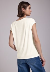 Cremefarvet t-shirt med korte ærmer og rund halsudskæring, i en afslappet pasform og lavet af blødt bomuldsstof, parret med blå denimjeans.