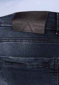 Tmavě modré džíny se koženou nášivkou s embosovaným nápisem "GABBIANO", viditelným švem a hladkým povrchem. Zahrnuta také detail zadní kapsy.