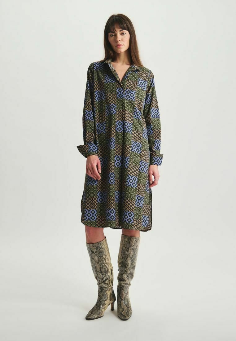 Robe à manches longues verte avec des motifs floraux et géométriques bleus, présentant un col et une coupe décontractée. Associée à des bottes en imprimé serpent.