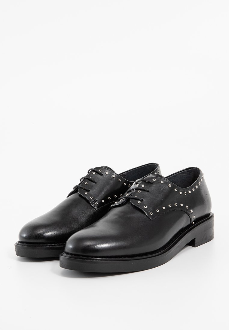 Chaussures en cuir noir avec des bouts arrondis, des semelles plates et des studs en argent décoratifs le long des bords supérieurs. Présente un design classique à lacets.